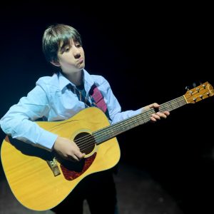 teenage boy holding a guitar on stage
