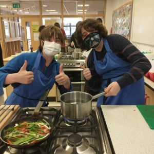 two boys standing in front of a stove wearing covid masks