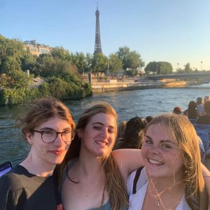 3 students smiling on a boat with the Eiffel Tower in the background